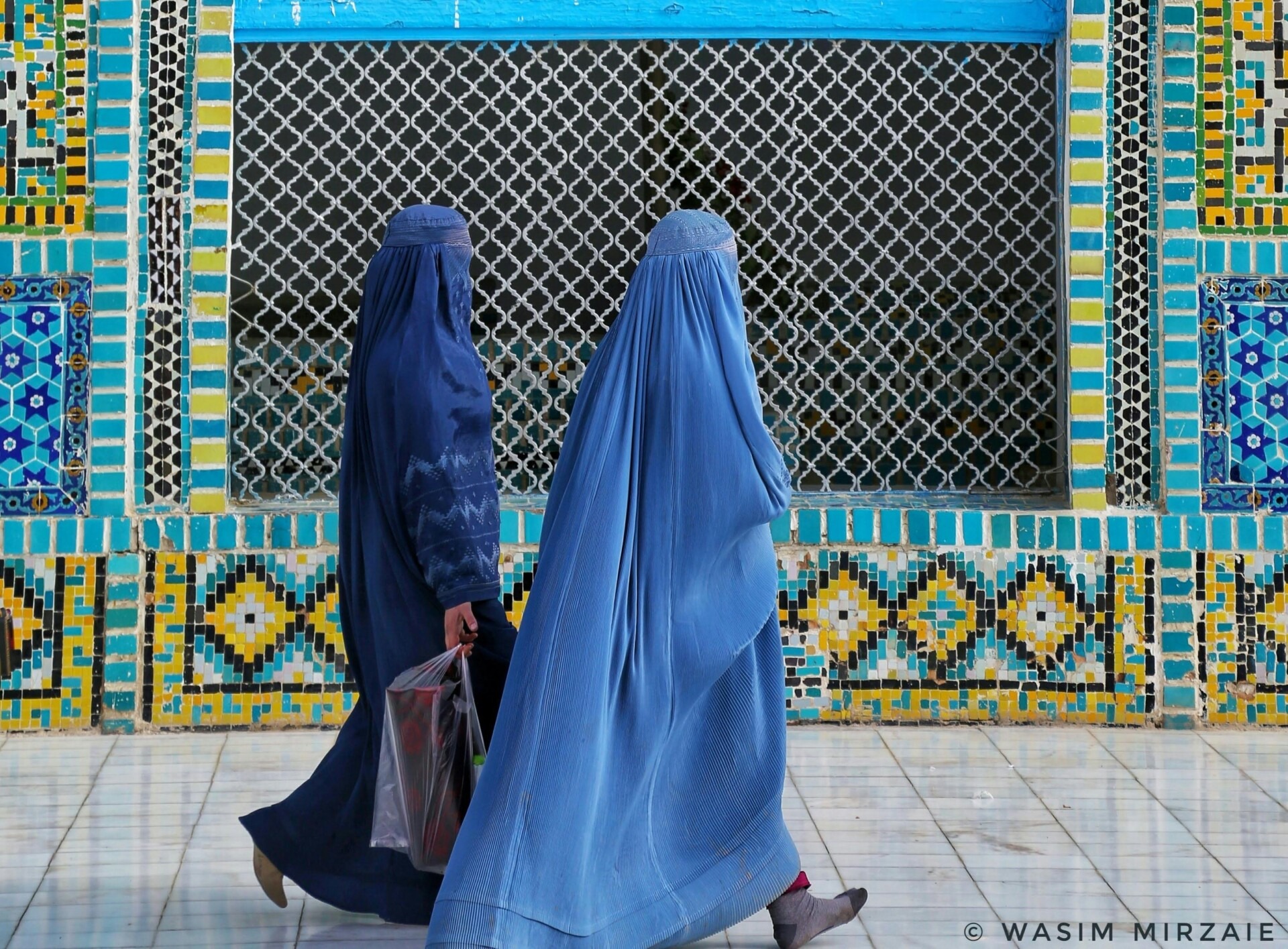 Two women wearing burqas walked in front of a blue mosaic wall