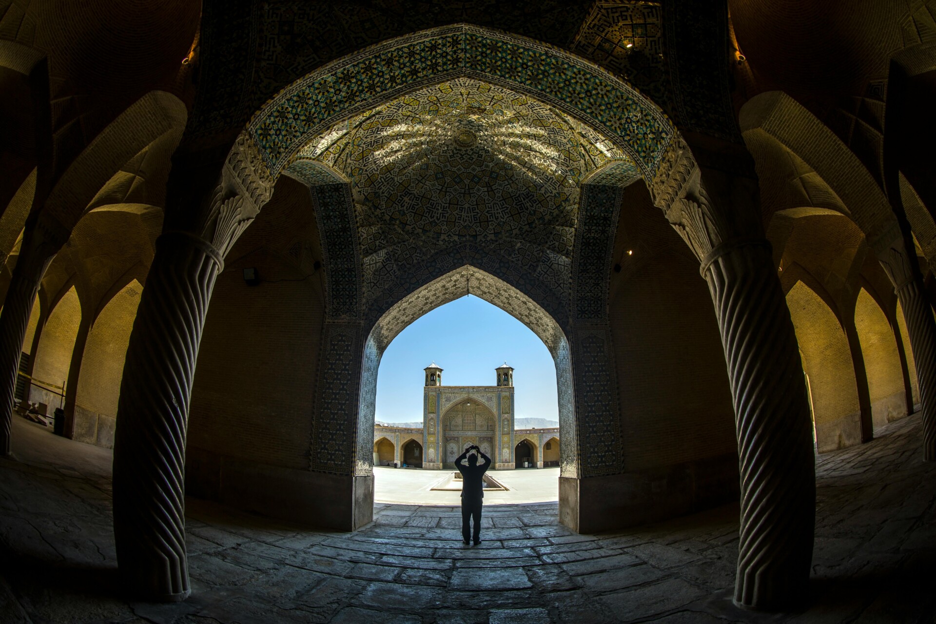 Photographic image of a lone man exiting the interior of a mosque that is heavily shadowed