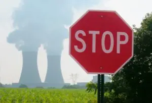A road stop sign in front of a nuclear power plant in the distant background. Smokes billows from the nuclear reactors.
