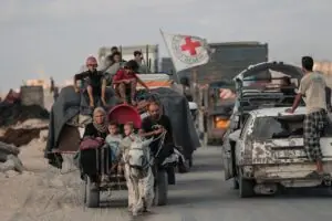 Displaced Palestinians moving in a convey via horse and cart. A Red Cross flag flies in the background.