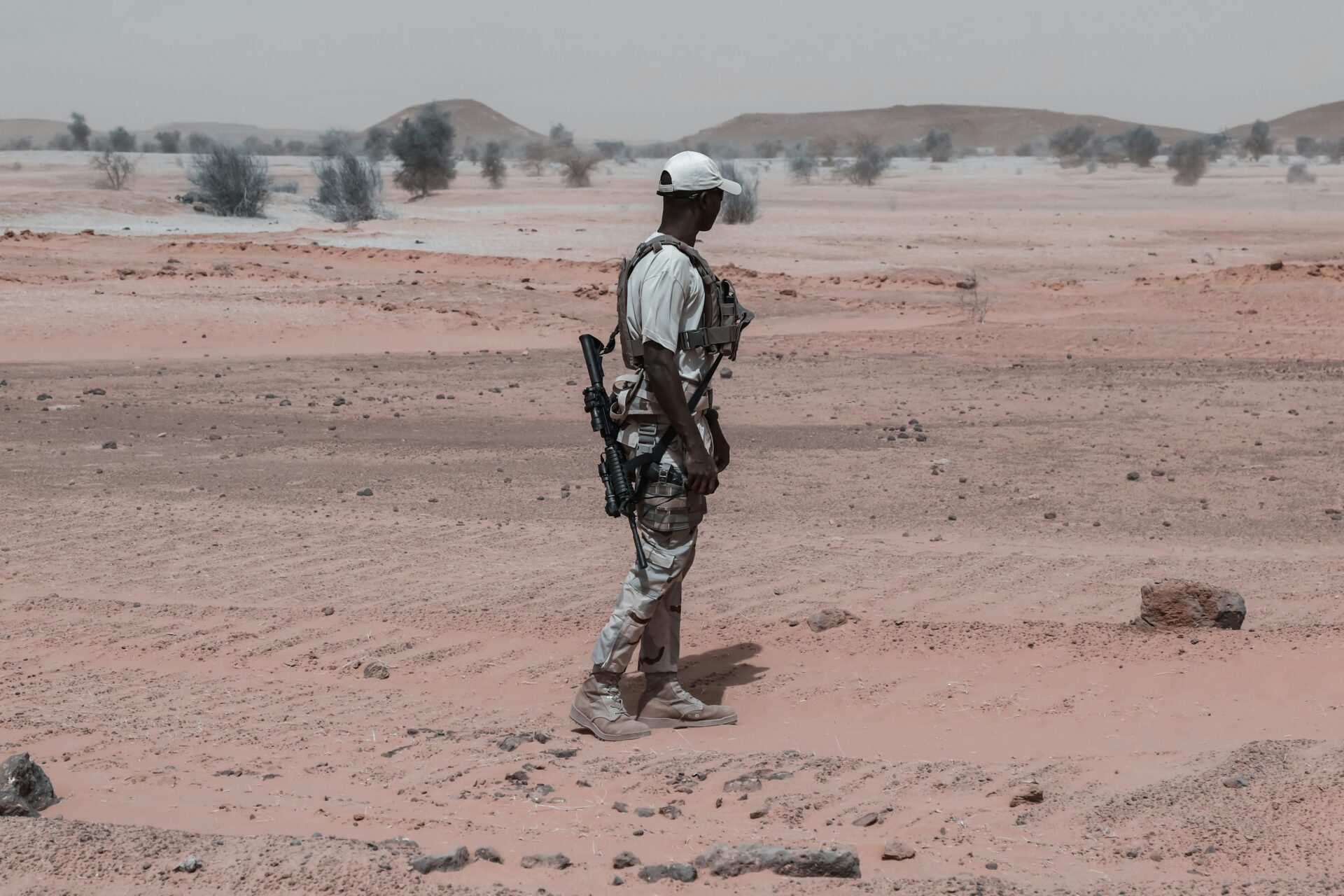 Solider with his back turned to the camera standing in the Sudan desert with a riffle over his shoulder standing into the distance.