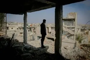 Man stands at the edge of his demolished home looking out at the destruction caused by the bombing to his hometown.