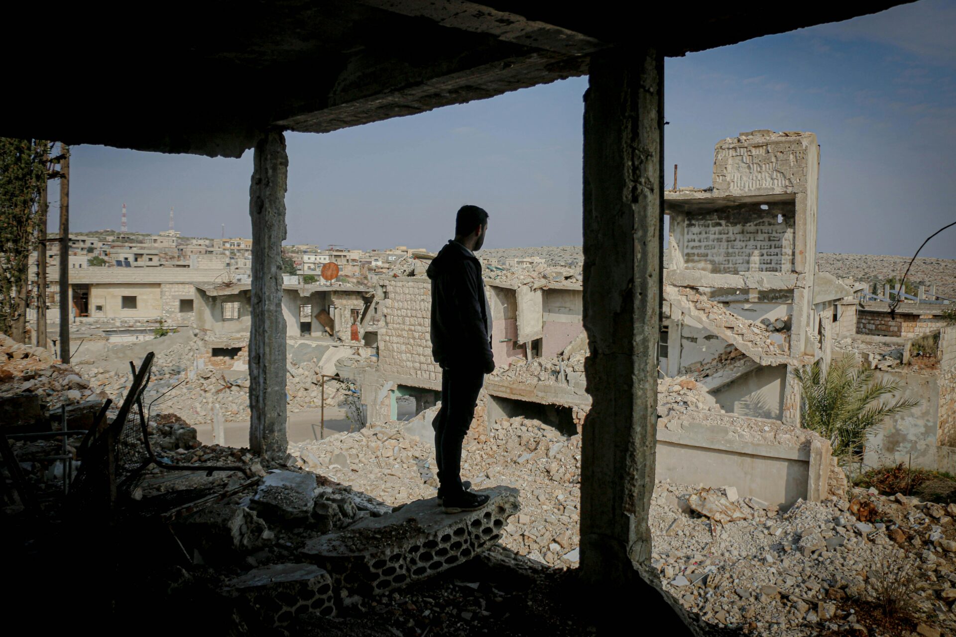 Man stands at the edge of his demolished home looking out at the destruction caused by the bombing to his hometown.
