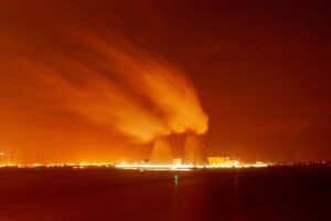 Two cooling towers emitting steam against an orange night sky