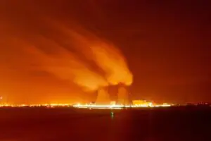 Two cooling towers emitting steam against an orange night sky