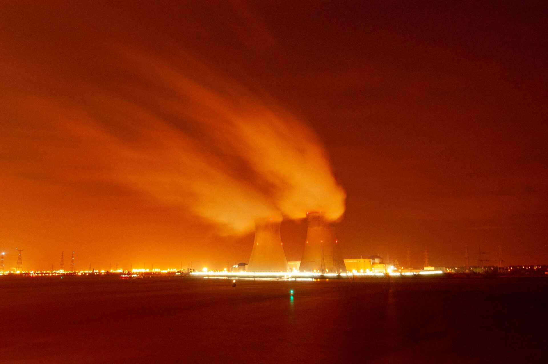 Two cooling towers emitting steam against an orange night sky